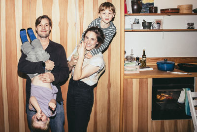 Portrait of smiling parents playing with sons while standing in kitchen at home