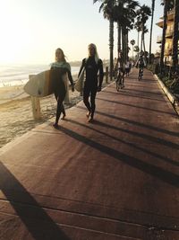 People on footpath by sea against sky in city