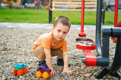 Little toddler boy playing with cars on pebbles on the playground. boy two or three years old