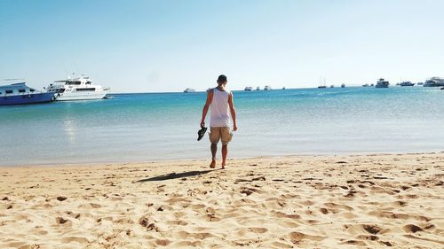 Rear view of woman walking on beach against clear sky