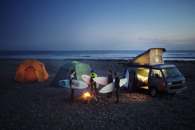 Friends with surfboard camping at beach against sky