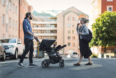 Full length side view of parents with baby boy and stroller crossing city street