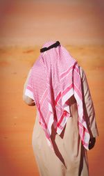 Rear view of man in traditional clothing standing at desert during sunny day
