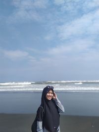 Young woman standing on beach against sky