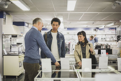 Mature owner talking to male and female customers in electronics store