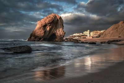 Rock formation on beach against cloudy sky