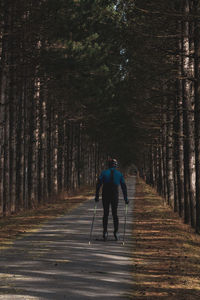 Rear view of woman skating on road amidst trees