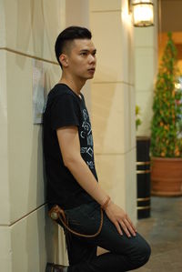 Side view of thoughtful young man looking away while leaning on tiled wall