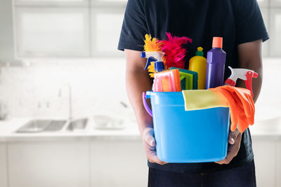 Midsection of man holding multi colored cleaning equipment at home