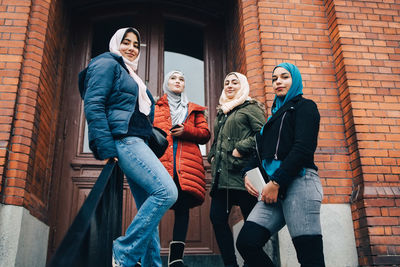 Full length of friends standing against brick wall