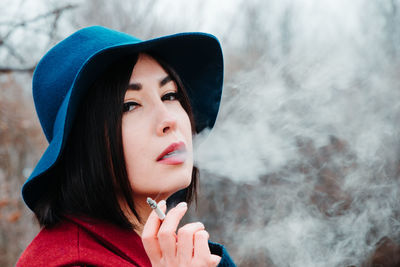 Portrait of beautiful young woman wearing hat smoking cigarette