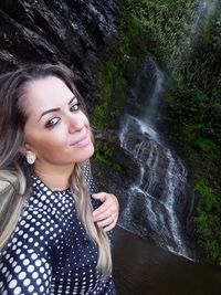 Portrait of beautiful young woman against waterfall