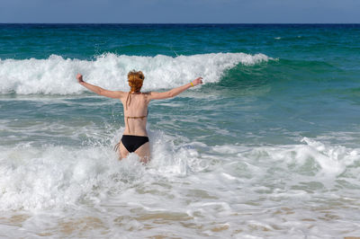 Rear view of carefree woman with arms outstretched standing in sea