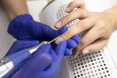 The manicurist cuts the cuticles of the nails with an electric milling machine wearing blue latex