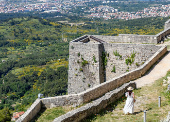 Young woman in white dress standing at klis fortress overlooking coastal city of split in croatia