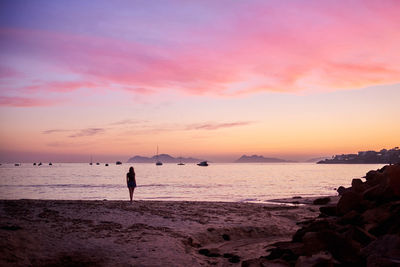 Rear view of woman standing on beach against sky during sunset