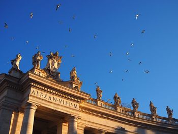 Low angle view of sacred statues and flying birds over st. peter's square