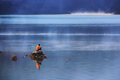 Man fishing in lake while sitting on rock