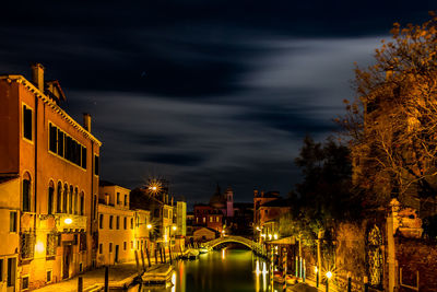 Illuminated buildings by street against sky at night