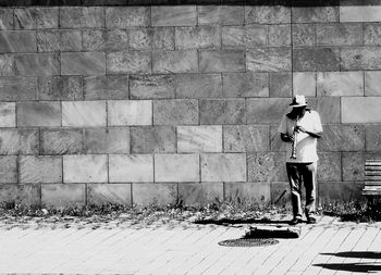 Man standing on footpath against wall