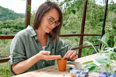 Woman sowing medicinal or aromatic herbs in clay pot on balcony. home planting and food growing. 