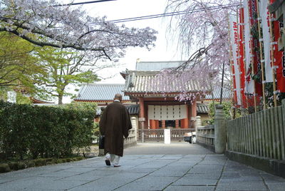 Rear view of man walking on footpath amidst buildings