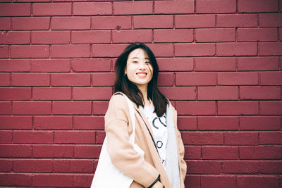 Portrait of smiling young woman standing against brick wall