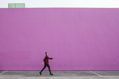 Full length of woman jumping on footpath against pink wall