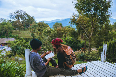 Rear view of people sitting by plants against trees