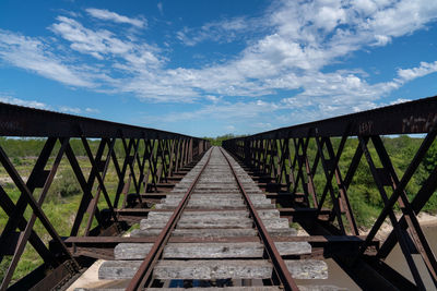 Abandoned iron railway bridge over a stream with a sky and clouds background