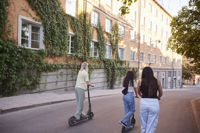 Young female friends spending time together outdoors riding electric scooters