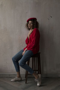 Young woman looking away while sitting on chair against wall