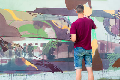 Rear view of street artist painting graffiti on wall