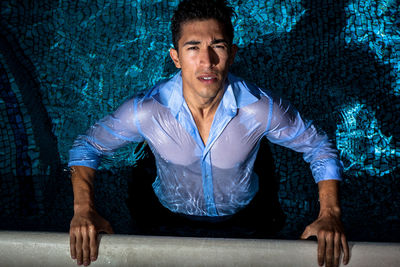 Portrait of young man sitting against wall