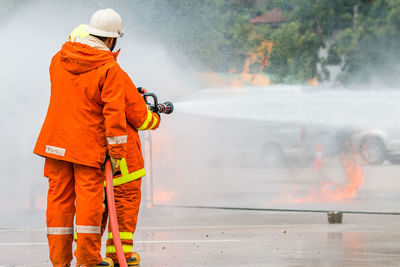 Rear view of firefighter spraying water on fire while standing at street