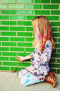 Side view of girl kneeling by green wall