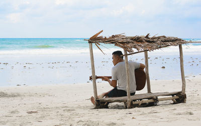 Rear view of man playing guitar on beach against sky