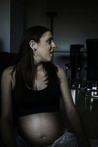 Young thoughtful pregnant lady in sportswear and sitting on floor in room