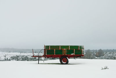 Trailer on snow covered field against clear sky