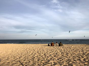 Rear view of people sitting at beach against sky