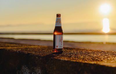 Close-up of water bottle on beach against sky during sunset