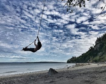 Upside down image of swing at beach against sky