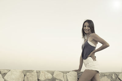 Portrait of beautiful woman standing by wall against sky