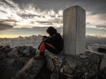 Rear view of people sitting on rock against sky