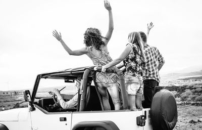 Friends enjoying in off-road vehicle against sky