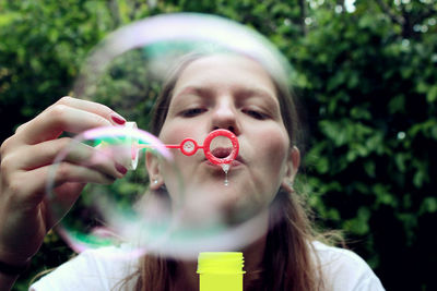 Portrait of woman holding wand seen through bubble against plants