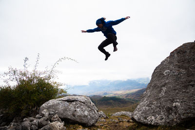 Man jumping on rock against sky