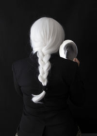 Rear view of woman holding mirror while standing against black background
