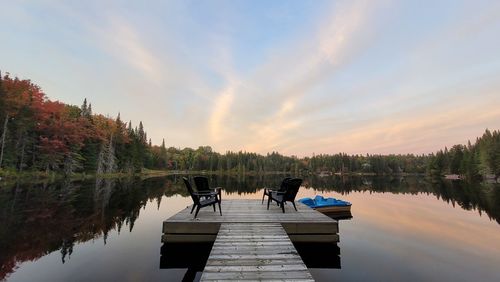 Rear view of woman sitting on pier over lake against sky during sunset