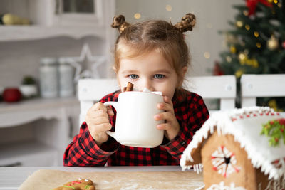 Portrait of cute girl holding coffee cup while sitting on table